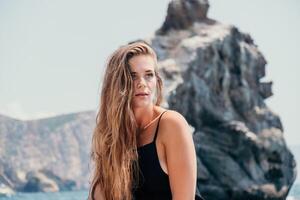 Woman summer travel sea. Happy tourist in hat enjoy taking picture outdoors for memories. Woman traveler posing on the beach at sea surrounded by volcanic mountains, sharing travel adventure journey photo