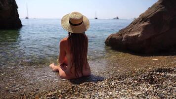 mujer viaje mar. contento turista en sombrero disfrutar tomando imagen al aire libre para recuerdos. mujer viajero posando en el playa a mar rodeado por volcánico montañas, compartiendo viaje aventuras viaje. video