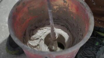 Builder Mixes Solution in Bucket. Plaster. Construction Site. Rotating Nozzle. Cement. Putty. Construction Mixture Diluted with Water. Renovation Work in Premises. Kneading. Close up, slow motion. video