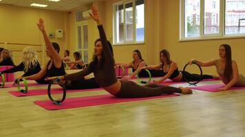 Group of middle aged women with fitness instructor in sportswear leggings and tops, exercising with the Magic Pilates ring on the yoga mat near the large mirror. Female fitness yoga routine concept video