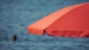 Red Beach Parasol umbrella on blue sky and sea background Red beach umbrella and blue sky. Summer beach vacations Waves of sea wash shoreline. Beach essentials on resort in summer view video