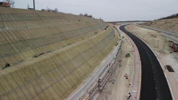 Workers reinforce the slope over the new road. Road construction in progress on slope nature canyon. Infrastructure development and logistics. Aerial drone shot video