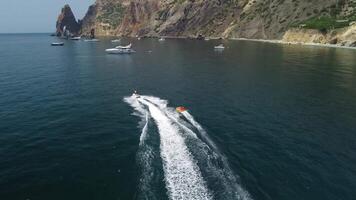 Happy people are going to swim on an air mattress behind a jet ski. Tourists ride the inflatable watercraft boat. Sea attraction. Jet ski skating people on a large Inflatable raft. Aerial copter view. video