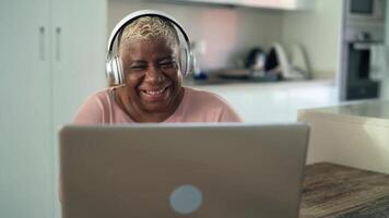 an older woman wearing headphones and smiling while using a laptop video