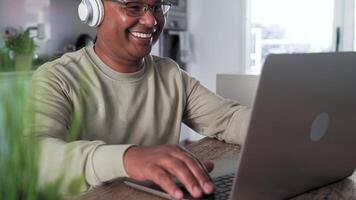 uma jovem homem vestindo fones de ouvido e sorridente enquanto usando uma computador portátil video