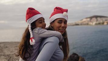 a woman and a child wearing santa hats on the beach video