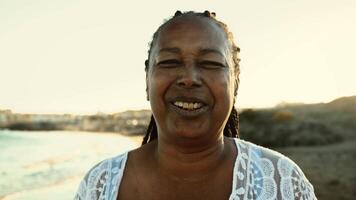 Happy African senior woman having fun smiling into the camera on the beach during summer vacation - Elderly people lifestyle concept video