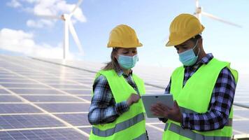 Young engineer working for alternative energy with wind turbine and solar panel while wearing face mask during corona virus outbreak - Innovation and green power concept video