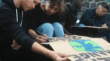 diverso activistas con diferente años y etnia preparando protesta pancartas en contra ambientes desastres - global calentamiento concepto video