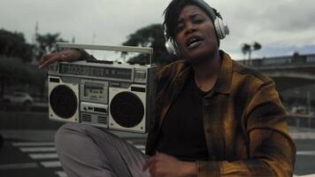 Happy African girl having fun listening to music with headphones and vintage boombox stereo video