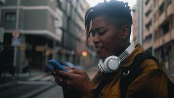 feliz africano mulher usando Móvel Smartphone enquanto ouvindo música com sem fio fones de ouvido video