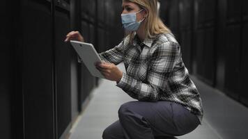 een vrouw vervelend een masker en Holding een tablet computer in een server kamer video