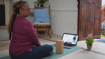 a woman is sitting on a yoga mat with a laptop video