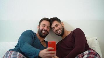 deux Hommes dans pyjamas sont souriant tandis que à la recherche à une cellule téléphone video