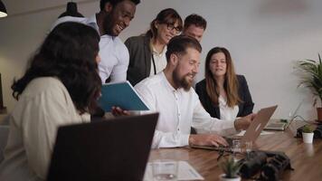 a group of people in a meeting room looking at a laptop video