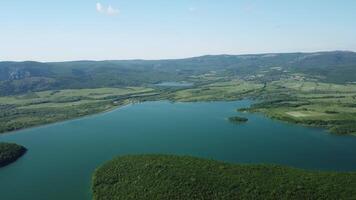 aéreo ver en agua reservorio a montaña Valle cubierto con verde primavera bosque. hermosa ver desde encima en suave azul superficie de montaña lago entre tierras altas. zumbido punto de vista. nadie video