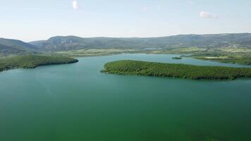 aéreo ver en agua reservorio a montaña Valle cubierto con verde primavera bosque. hermosa ver desde encima en suave azul superficie de montaña lago entre tierras altas. zumbido punto de vista. nadie video