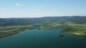 aérien vue sur l'eau réservoir à Montagne vallée couvert avec vert printemps forêt. magnifique vue de au dessus sur lisse bleu surface de Montagne Lac parmi hauts plateaux. drone point de voir. personne video