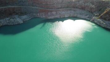 aéreo parte superior ver en a cielo abierto minería cantera con inundado abajo, turquesa superficie de el lago. cantera estanque descuidado con verde plantas y claro turquesa agua video