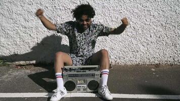 a man sitting on the ground with his arms up and a boombox video