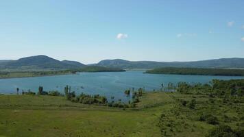 aérien vue sur l'eau réservoir à Montagne vallée couvert avec vert printemps forêt. magnifique vue de au dessus sur lisse bleu surface de Montagne Lac parmi hauts plateaux. drone point de voir. personne video