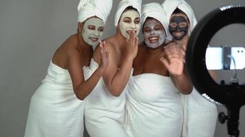 quatro mulheres dentro toalhas com facial máscaras em posando dentro frente do uma câmera do telefone video