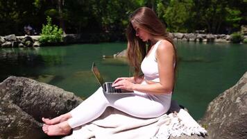 Well looking middle aged woman typing on laptop keyboard outdoors near lake with swans in the park. Close up woman hands writing on computer. Freelance, digital nomad, travel and holidays concept. video