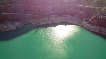 aereo superiore Visualizza su a cielo aperto estrazione cava con allagato parte inferiore, turchese superficie di il lago. cava stagno coperto di vegetazione con verde impianti e chiaro turchese acqua video