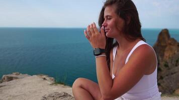 Woman travel portrait. Happy woman with long hair looking at camera and smiling, sharing her travel stories with friends. Close up portrait woman posing on a volcanic rock high above sea. Slow motion video