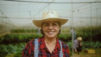 a woman in a hat is smiling in a greenhouse video