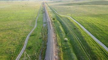 antenn se av en järnväg Spår skärande genom en frodig fält av grön vete i landsbygden. fält av vete blåser i de vind tycka om grön hav. agronomi, industri och mat produktion. video