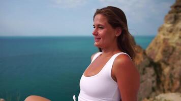 mulher viagem retrato. feliz mulher com grandes cabelo olhando às Câmera e sorridente, partilha dela viagem histórias com amigos. fechar acima retrato mulher posando em uma vulcânico Rocha Alto acima mar. lento movimento video