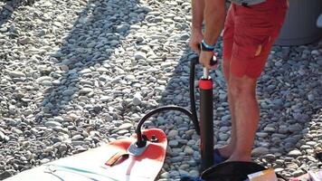 Man Inflates Standup Puddle Board. Person pumping on beach close up shot of pump and person hands in focus while constantly pumping. Slow motion video