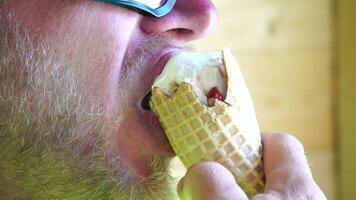 hombre comiendo hielo crema. de cerca retrato de joven hipster hombre en gafas de sol comiendo hielo crema en verano caliente clima en el playa, tener divertido y bueno humor. video