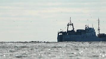 Fishing boat trawler catches fish while sailing on sea. A commercial fishing boat on the horizon in a distance sail to catch school of fish on calm sea surface in summer. Commercial catch of sea fish. video