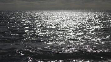 abstrakt hav sommar hav solnedgång natur bakgrund. små vågor på gyllene vatten yta i rörelse fläck med gyllene bokeh lampor från Sol. Semester, semester och rekreation. väder och klimat förändra video