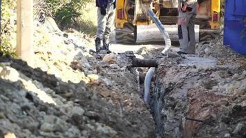 Plastik Rohre gelegt im Gräben. Arbeitskräfte sind Installation Wasser Pipeline unter ein Stadt Straße im ein Graben. Neu Pipeline im ein Prozess von Gebäude, unter Konstruktion. Arbeitskräfte sind Verlegung Pipeline. schließen oben video