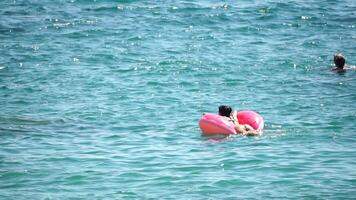 verano vacaciones mujer flotadores en un inflable rosquilla colchón, un agua juguete nadar anillo. positivo contento mujer relajante y disfrutando familia verano viaje Días festivos vacaciones en el mar. lento movimiento video