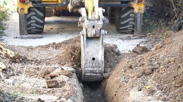 Excavator digs a trench to lay pipes. Close up of an excavator digging a deep trench. An excavator digs a trench in the countryside to lay a water pipe. Slow motion video