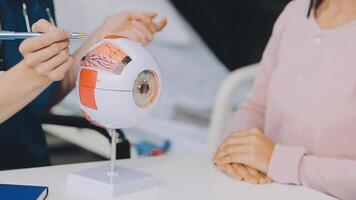 close up of asian female doctor wearing face mask is showing eyeball model and explaining about eyes disease to elder senior man patient in hospital video