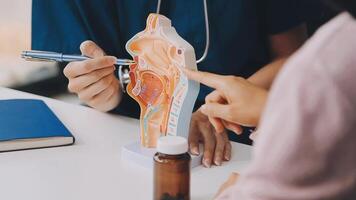 asian female doctor wearing face mask is showing a rectal model and explaining to elder senior man patient in hospital video