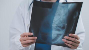 qualificato donna medico nel bianca uniforme controllo raggi X film, diagnosticare paziente lesione, sorridente calma e in piedi isolato su studio sfondo con copia spazio. assistenza sanitaria e medico assicurazione concetto video