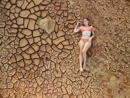 Aerial portrait of beautiful young lady in bikini lying on dry cracked red soil. arid, cracked red soil drought and arid climate conditions. Climate and weather change. photo