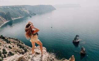 Woman travel sea. Happy tourist enjoy taking picture outdoors for memories. Woman traveler looks at the edge of the cliff on the sea bay of mountains, sharing travel adventure journey photo