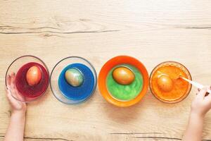 Hands of a girl child coloring festive Easter eggs with colorful dyes on the table at home photo