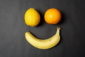 Oranges, bananas, and lemons form a smile with a black background. photo