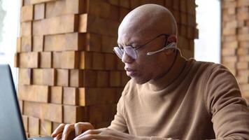 An african american man with a serious expression works with a laptop and documents at home. Pandemic. Lockdown video