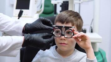 le ophtalmologiste sélectionne lentilles pour le garçon par veux dire de une procès Cadre pour sélection de lentilles video