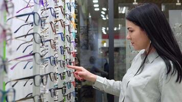 Young caucasian woman choosing glasses in optics store video