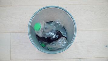 An empty trash can contains five bent plastic bottles and one green glass bottle of beer. Mixed garbage. Sorting and processing of plastic and glass waste. Garbage sorting. Recycling video